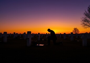 Fototapeta premium Silhouette of person kneeling at cemetery with crosses during sunset with orange and purple sky view