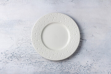 Empty white ceramic plate on light textured background, top view for food mockup or menu design...