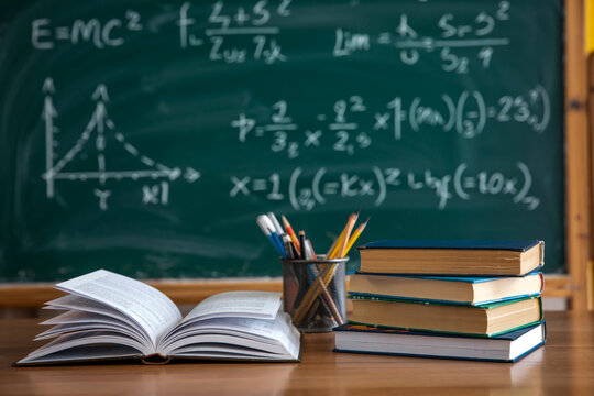 A photograph of a classroom setting with a green chalkboard in the background covered in white mathematical formulas and equations