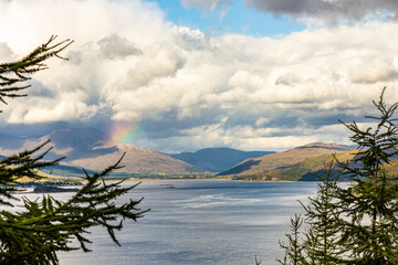 Scenic Highland Lake Surrounded by Mountains with Rainbow and Dramatic Clouds