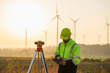 A field engineer surveys the land at sunset, with wind turbines behind as technology meets clean energy.