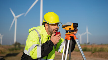 Surveying the land with high-precision tools, a field engineer works against a backdrop of wind turbines-where technology meets clean energy innovation.