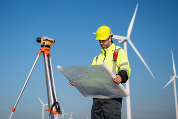 Surveying the land with high-precision tools, a field engineer works against a backdrop of wind...