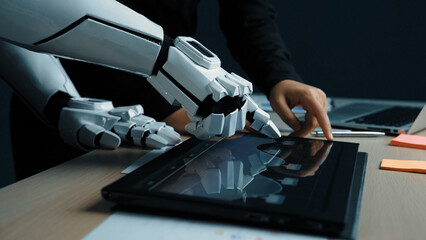 A robotic hand and a human hand work together on a sleek touchscreen device in a modern office,...