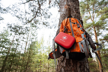 A bright orange backpack with a first aid kit is nestled in a tranquil forest, blending adventure...