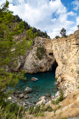 Majestic coastal cliffs embrace a serene turquoise cove at midday in a hidden paradise