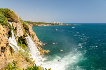 Majestic waterfall cascading into turquoise sea under bright blue sky on vibrant summer day