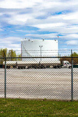 Industrial Oil Storage Tank With Tanker Trucks Behind a Fenced Area