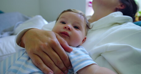 Baby resting on mother's chest, turning head and yawning, creating a peaceful and tender moment in...