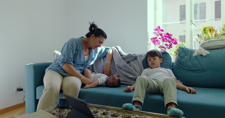 Close-up of a mother gently interacting with her baby as her son relaxes next to them on a couch, cozy family moment