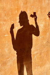 Shadow of a person holding three rectangular cards cast sharply on a textured ochre wall with...