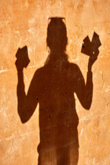 Silhouette of a person holding cards in both hands against a textured ochre wall with visible...