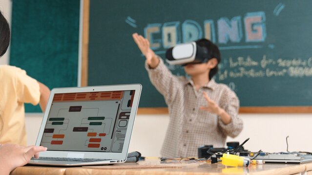Asian boy wearing VR headset to enter metaworld at table with electronic board while girl coding system. Group of diverse student working together to develop program and writing code. Pedagogy. - Powered by Adobe