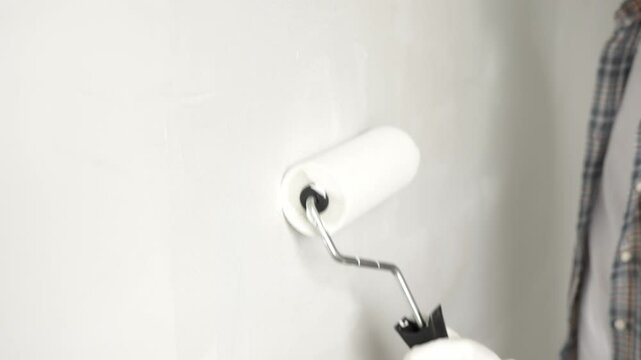 Close up focusing on gloved hand rolling white paint across wall surface, applying smooth, even coating during residential interior painting renovation