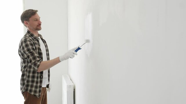 Professional house painter wearing gloves painting a white wall with a paint roller, working on a home renovation project, creating a fresh and clean look