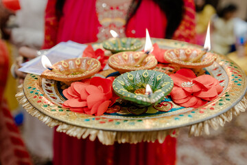 Decorative ceremonial tray holding lit diya lamps and flowers. Focus on the bright details of the...