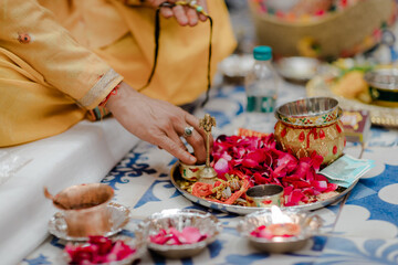 Ritualistic setup. The ceremony involves arranging small containers with rose petals, decorative tray with gold items, and a person dressed in a yellow ceremonial garment.