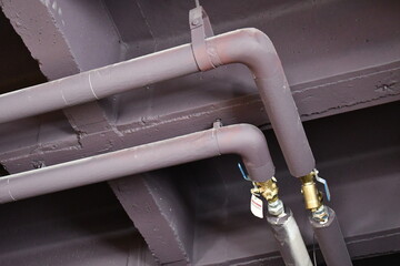 Utility pipes in school building ceiling. Two shutoff valves, pipes covered in insulation.