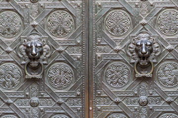 An antique door with intricate patterns and lion's head knockers, old and bold.