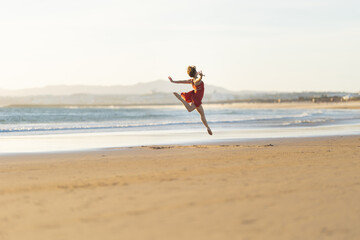 Ballerina performing a jump on the beach at sunset