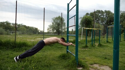 Obraz premium Young muscular athlete doing exercise on triceps at sport equipment outdoor. Male shirtless athlete working out at sport ground. Strong sporty man training at nature. Concept of healthy lifestyle