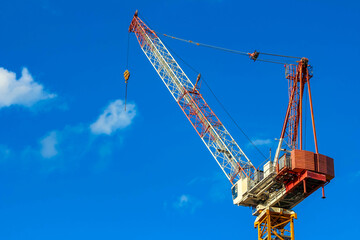 Naklejka premium Tall Construction Crane with Red Accents Against Vibrant Blue Sky at Urban Development Site