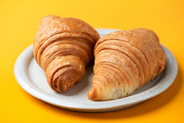 Two french croissants on a plate, yellow background