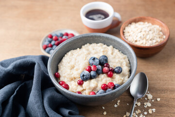 Breakfast oatmeal porridge with berries and cup of coffee, wooden table background