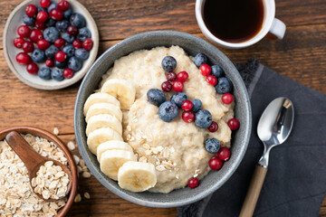 Breakfast oatmeal porridge with berries and cup of coffee, wooden table background