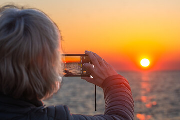 Close-up of a woman capturing a sunset with her smartphone—highlighting connection with nature, travel moments, and modern photography. Perfect for lifestyle, travel, and mobile tech content