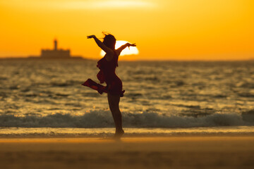 Fototapeta premium Dancer performing on the beach at sunset with lighthouse in background