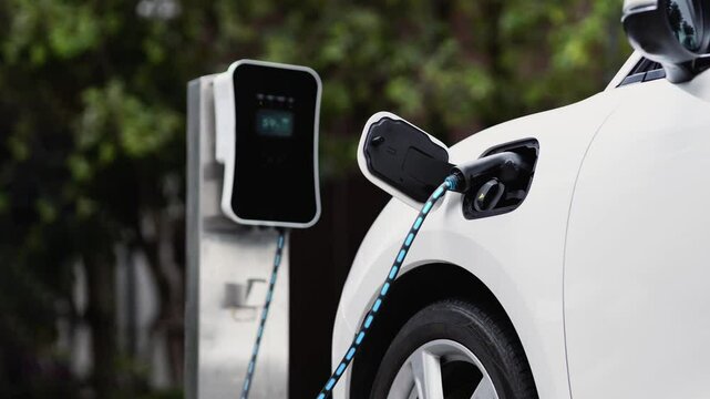 Electric car recharging battery by futuristic smart EV charger from eco clean energy charging station in natural green car park. Futuristic eco-friendly electric car using alternative energy. Peruse