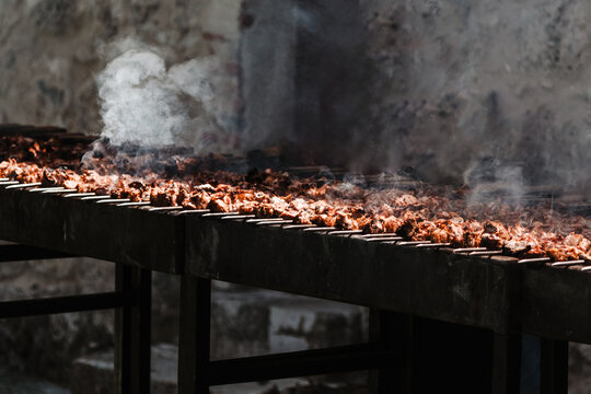 Gran parrilla con numerosos trozos de carne de lechazo cocin&aacute;ndose, con humo visible. Concepto de cocina tradicional en eventos. Catering