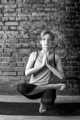 Young slender athletic girl in a turquoise tank top and dark leggings doing yoga against the background of a brick wall