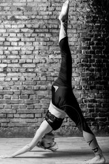 Young slender athletic girl in a turquoise tank top and dark leggings doing yoga against the background of a brick wall