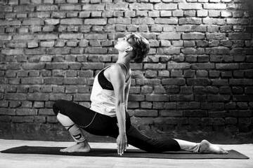 Young slender athletic girl in a turquoise tank top and dark leggings doing yoga against the background of a brick wall