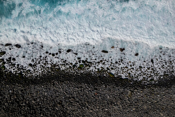 Top down view of Turquoise water waves hitting mossy boulders at Ponta do Sol, Madeira Island, Portugal