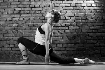 Young slender athletic girl in a turquoise tank top and dark leggings doing yoga against the background of a brick wall