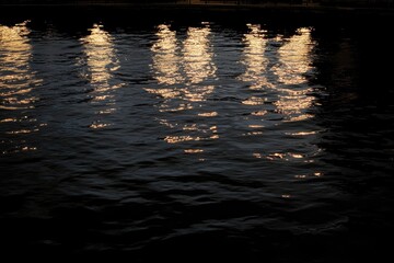 Reflections of lights on dark water.  Light patterns reflected in ripples of water