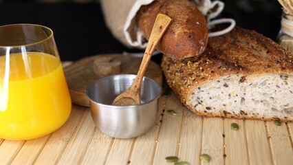 Freshly baked seeded bread in burlap sack, metal bowl with salt, wooden spoon, glass of orange...