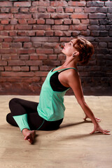 Young slender athletic girl in a turquoise tank top and dark leggings doing yoga against the background of a brick wall