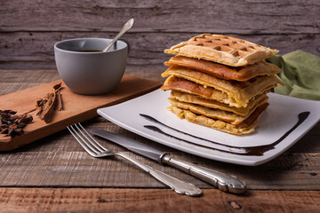 Stack of waffles and cup of coffee in rustic setting.