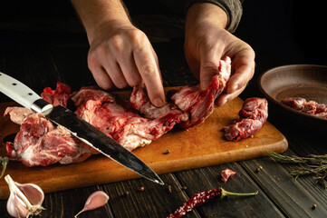 Hands skillfully prepare raw meat, separating cuts on a wooden board. Surrounding ingredients include garlic, chili, and fresh herbs, creating a rich cooking atmosphere
