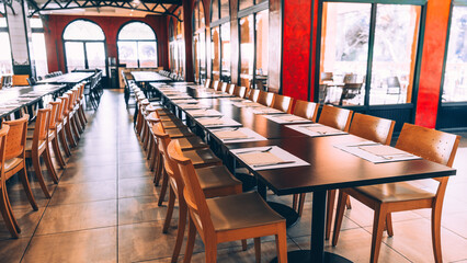 Elegant interior of a modern restaurant with long tables neatly set for a large group, creating a warm atmosphere with natural light and a vibrant red accent wall. ready for an event