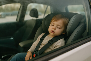 Child sleeping alone in a parked car. A small child sleeps alone in a car seat inside a parked car. View through the vehicle window in a parking lot.