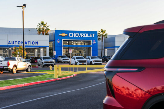 Chevrolet and Ford trucks are displayed at an AutoNation dealership, with a red SUV entering the foreground, showcasing auto retail layout, vehicle variety, and consumer access pathways.