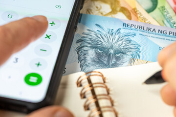 Philippines money. Counting on smartphone calculator, PHP symbol, Notes in notebook. Financial settlement, Household budget, Taxes, Philippine currency exchange rate, Enterprise financial analysis