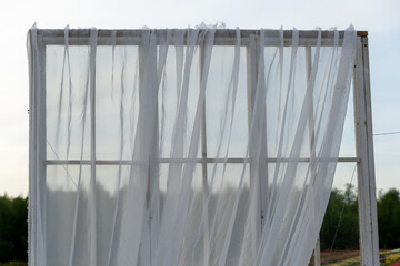 Open window frame with sheer white fabric, revealing natural outdoor landscape background during golden hour sunlight