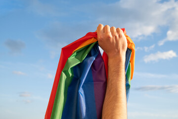 Hand Holds LGBTQ Flag on blue sky 
