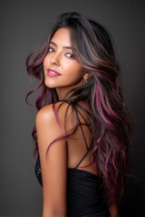 Stunning woman with flowing hair and subtle pink highlights posing gracefully against a dark backdrop in a fashionable outfit